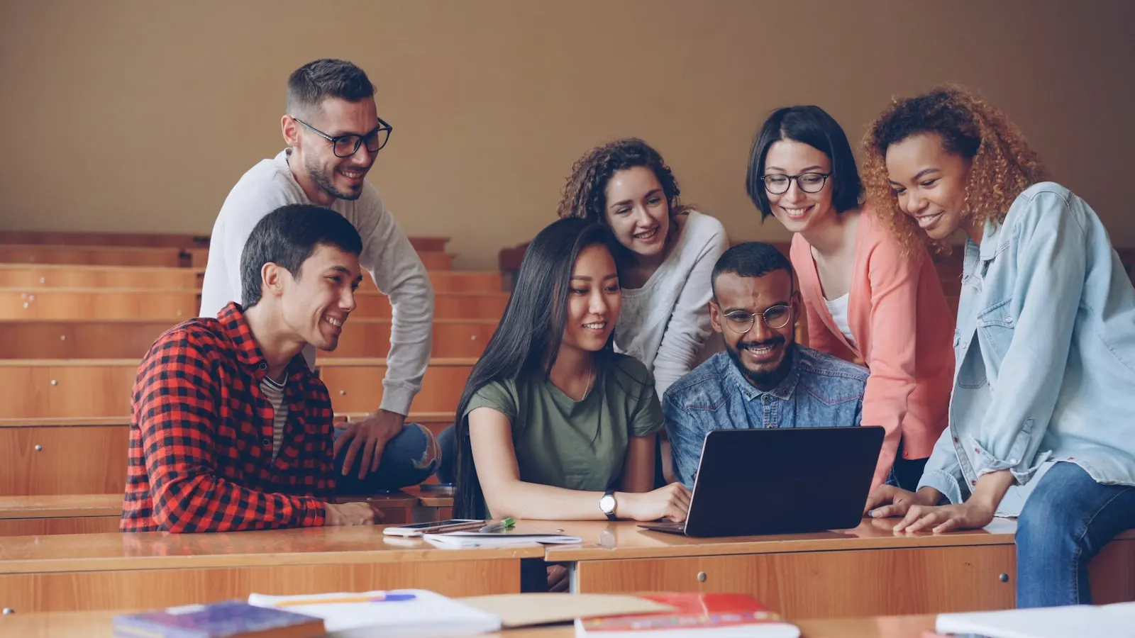 A diverse group of students collaborating around a laptop in a lecture hall