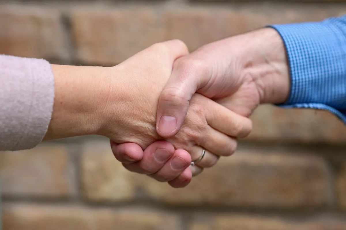 A handshake between two people in front of a brick wall